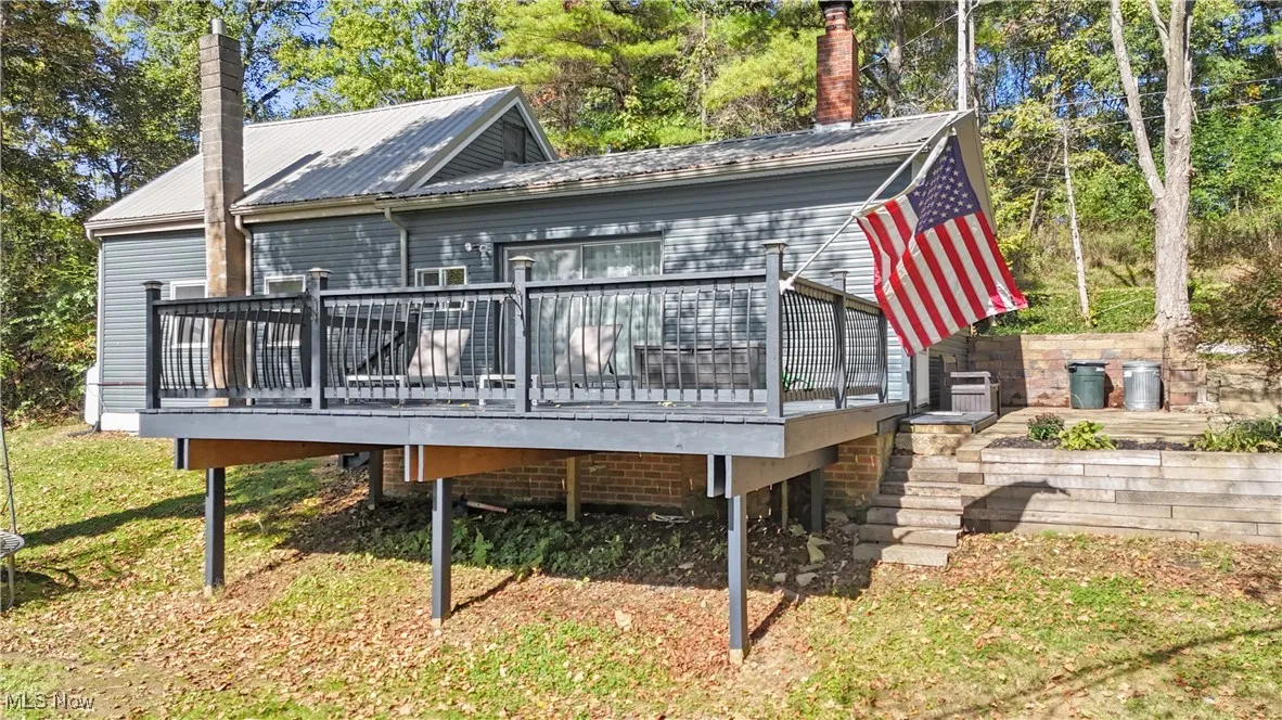Back of house with a deck, view of scattered trees, and a metal roof