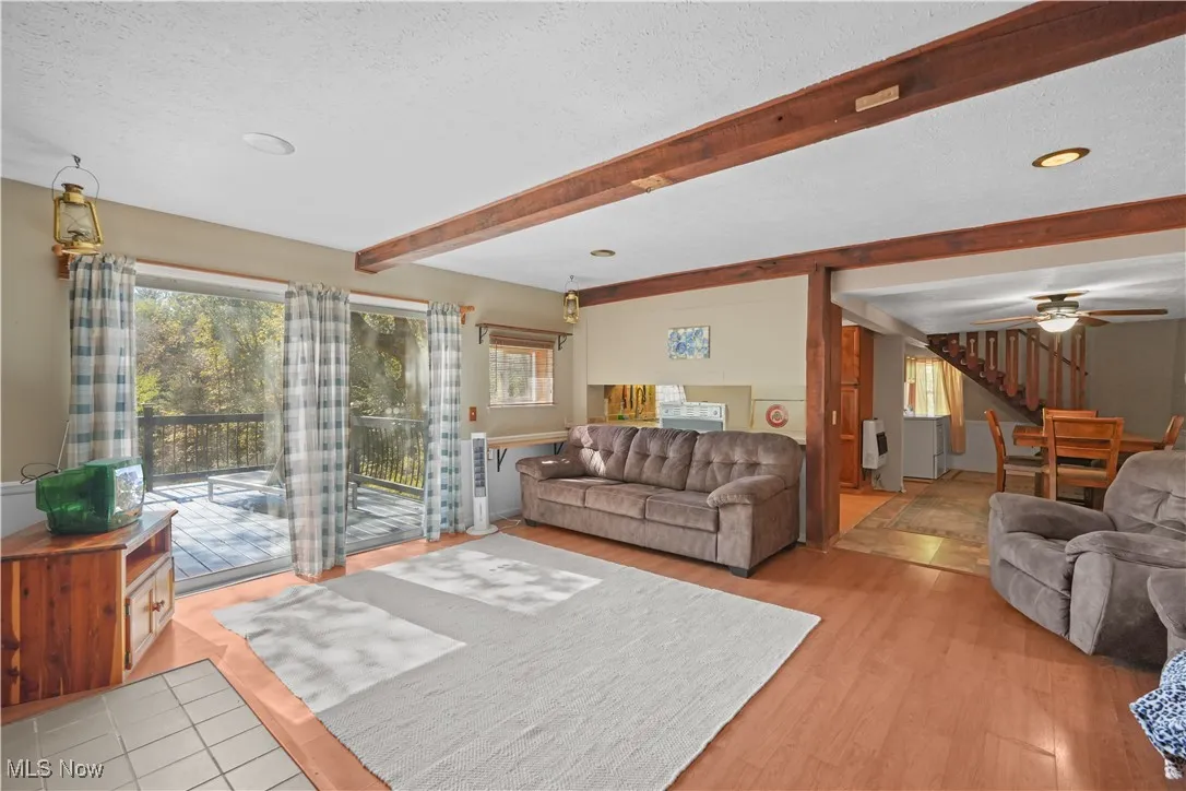 Living area featuring beam ceiling, a textured ceiling, stairway, light wood-style flooring, and a ceiling fan