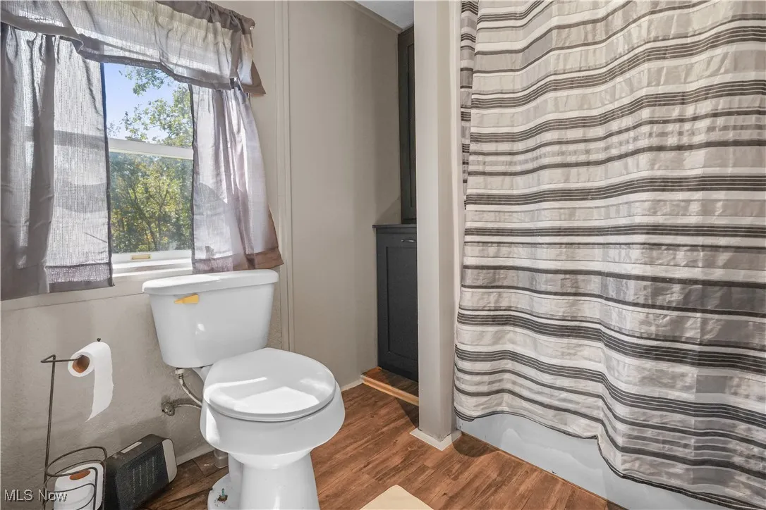 Bathroom with dark wood finished floors and shower / tub combo with curtain