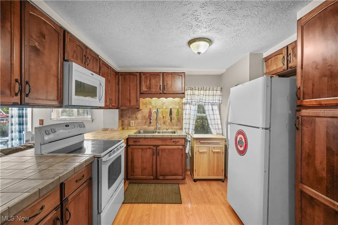 Kitchen featuring white appliances, light wood-type flooring, brown cabinets, a textured ceiling, and tile countertops
