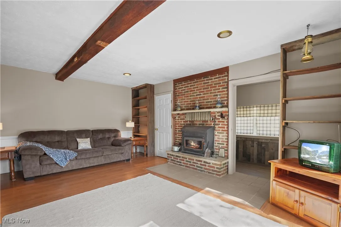 Living area featuring beamed ceiling, light wood-style flooring, and a brick fireplace