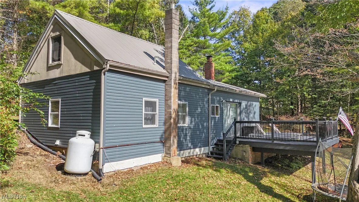 Rear view of house featuring view of scattered trees, a chimney, a wooden deck, a metal roof, and a yard