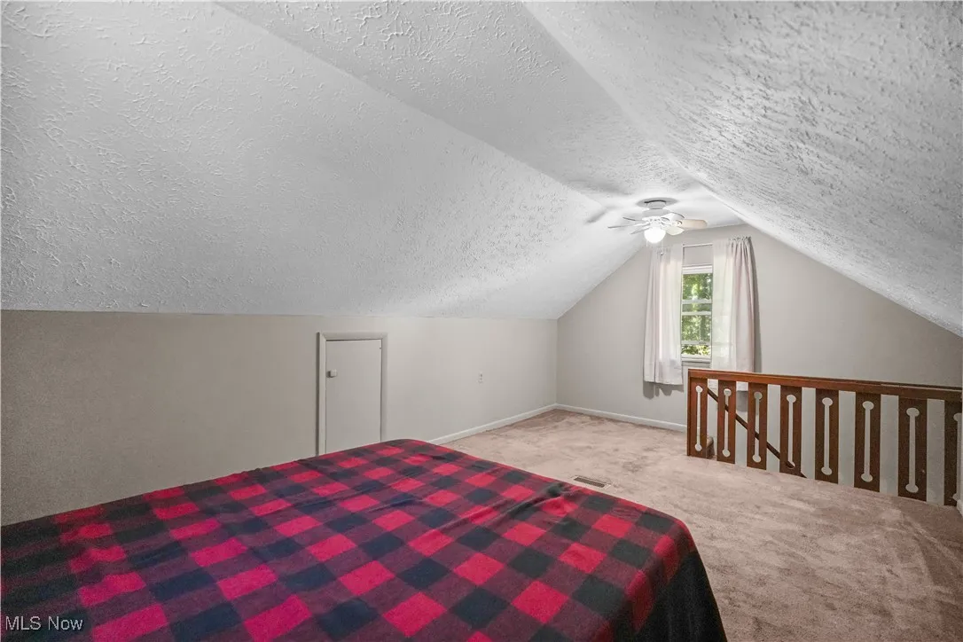 Unfurnished bedroom with carpet, ceiling fan, lofted ceiling, and a textured ceiling