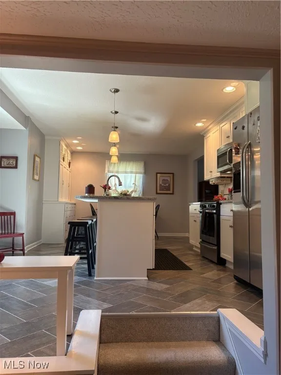 Kitchen featuring black range, fridge, white cabinetry, decorative light fixtures, and a breakfast bar