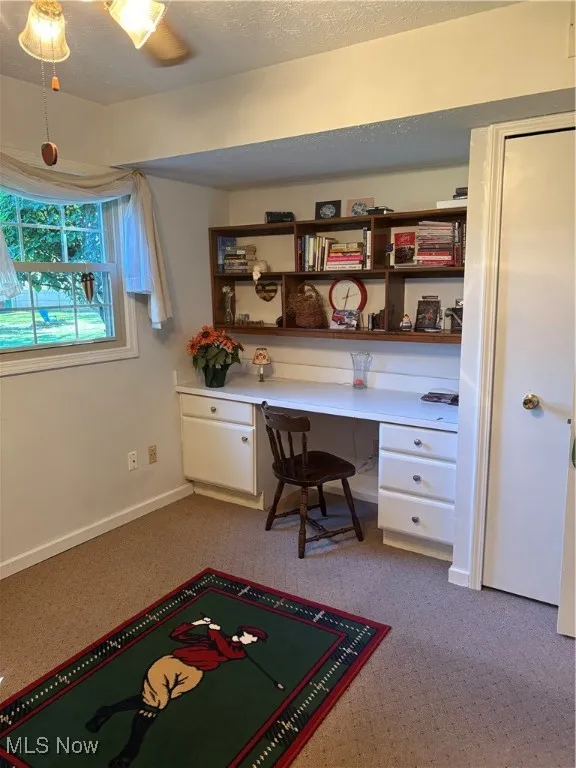 Home office featuring built in study area, light carpet, and a textured ceiling