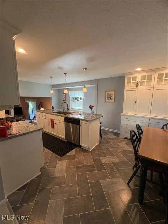 Kitchen with a kitchen island with sink, white cabinetry, decorative light fixtures, dishwashing machine, and light stone countertops