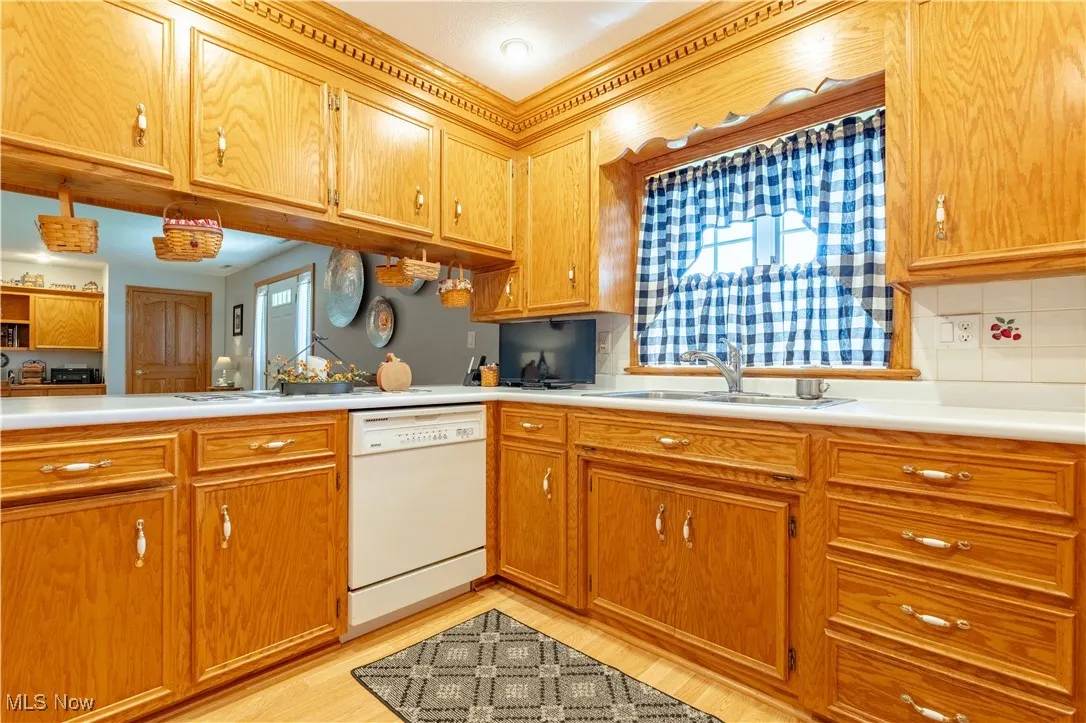 Kitchen featuring light countertops, dishwasher, light wood-style floors, brown cabinetry, and tasteful backsplash
