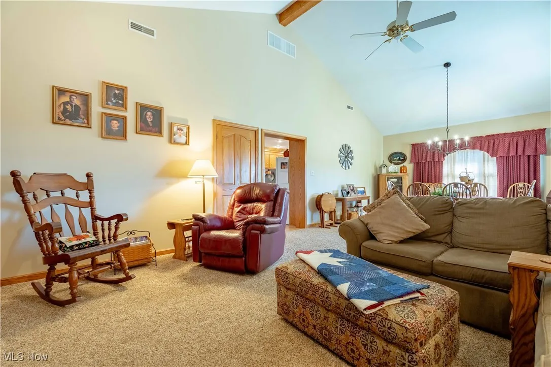 Carpeted living area with high vaulted ceiling, beam ceiling, a chandelier, and a ceiling fan