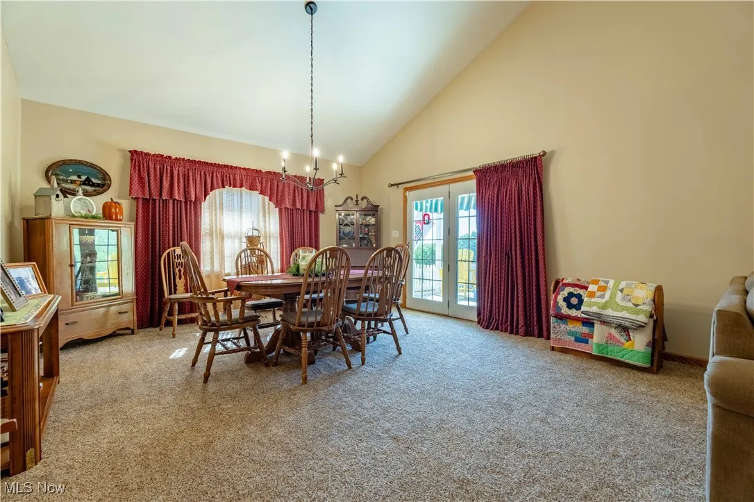 Dining area with high vaulted ceiling, light carpet, french doors, and a chandelier