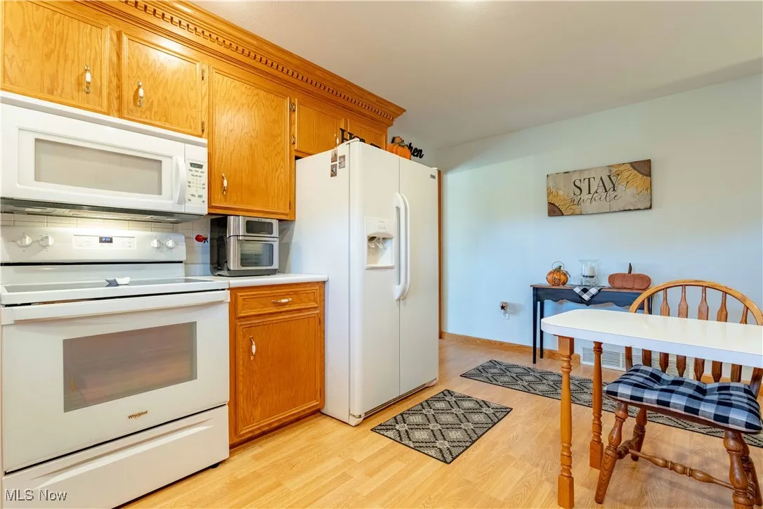 Kitchen featuring white appliances, light countertops, brown cabinetry, and light wood-style floors