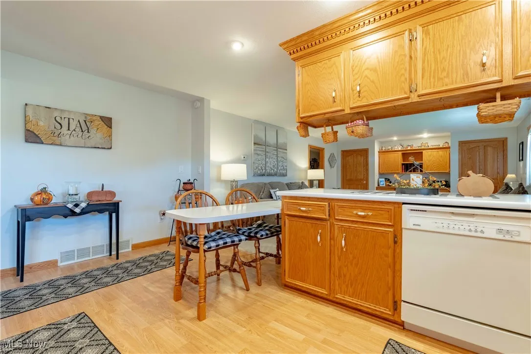 Kitchen with white dishwasher, light countertops, brown cabinets, light wood finished floors, and open floor plan