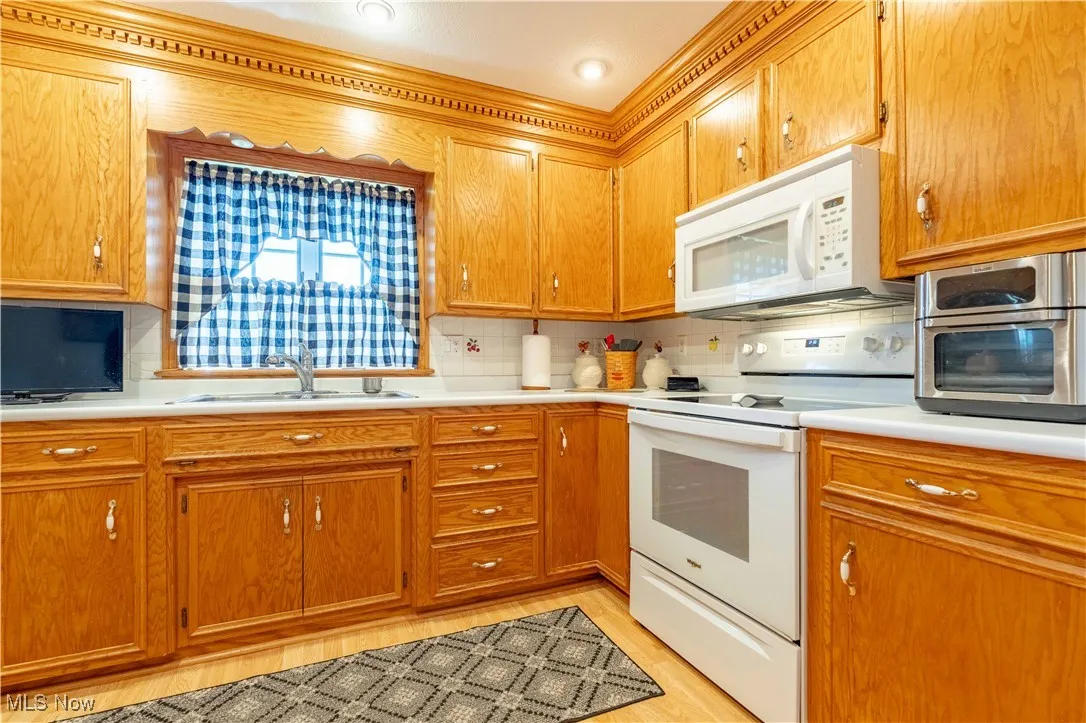 Kitchen with white appliances, light countertops, decorative backsplash, and brown cabinetry