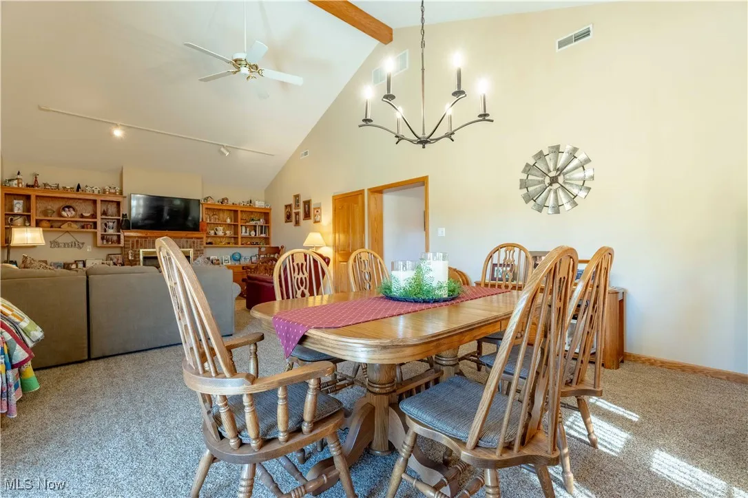 Dining area with high vaulted ceiling, beamed ceiling, ceiling fan, a chandelier, and light colored carpet