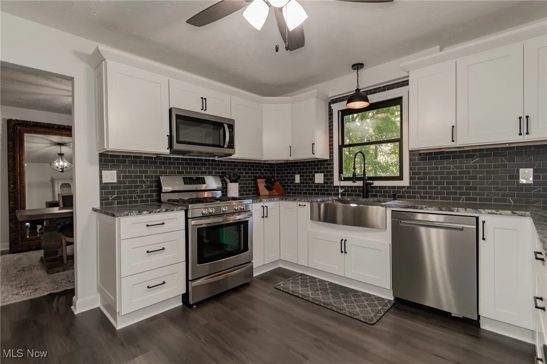 Kitchen featuring stainless steel appliances, decorative light fixtures, white cabinetry, and dark stone countertops
