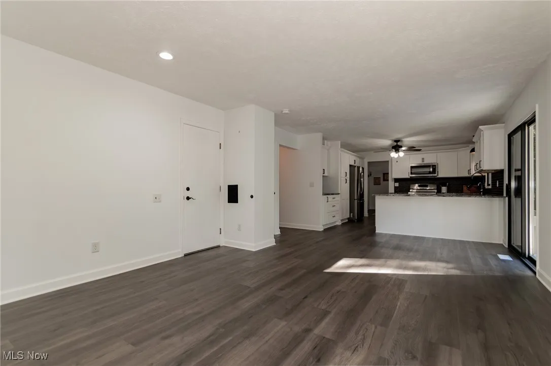 Unfurnished living room featuring dark wood-type flooring and ceiling fan