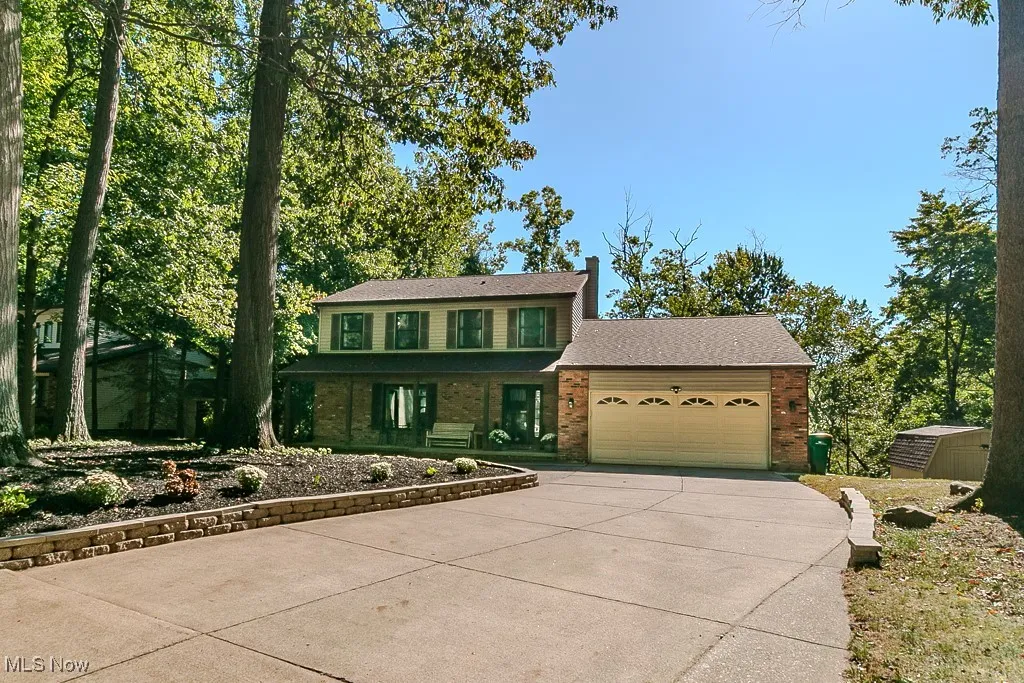 View of front of property with brick siding, concrete driveway, a garage, and a storage shed