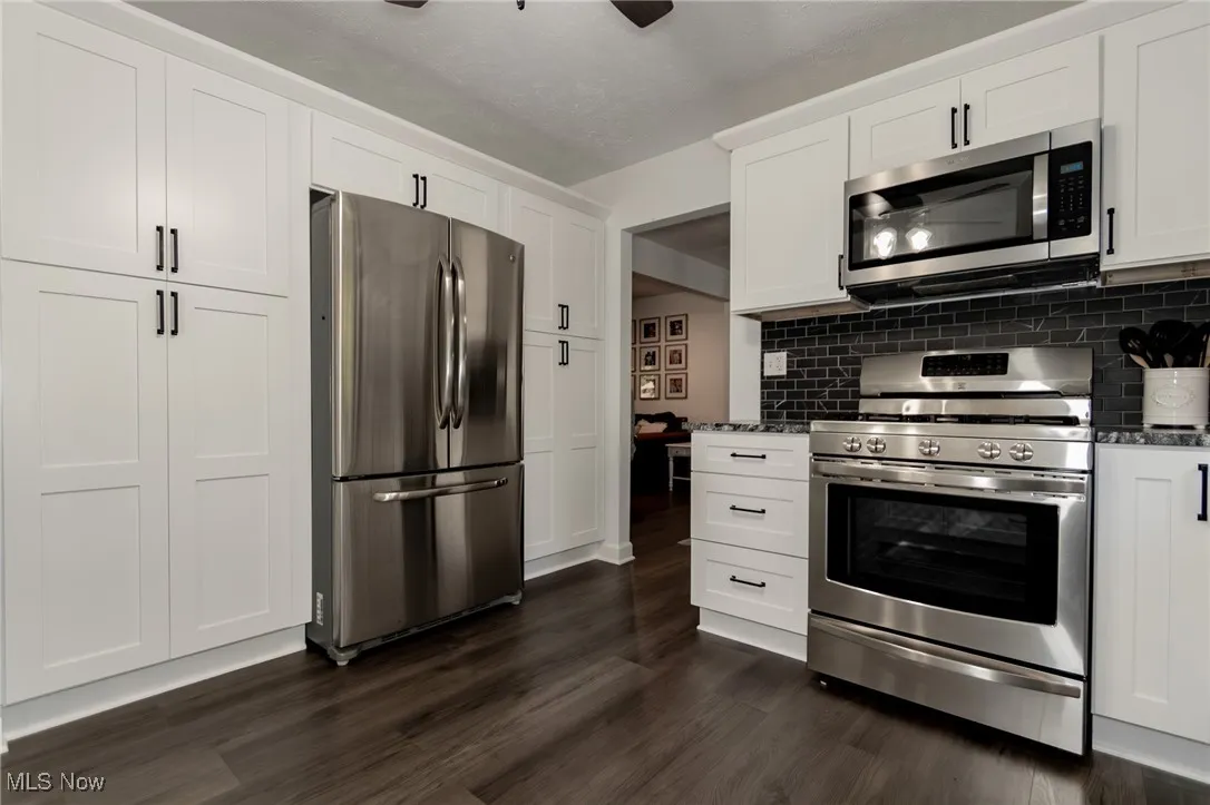 Kitchen with appliances with stainless steel finishes, white cabinetry, dark stone counters, and dark wood-style flooring