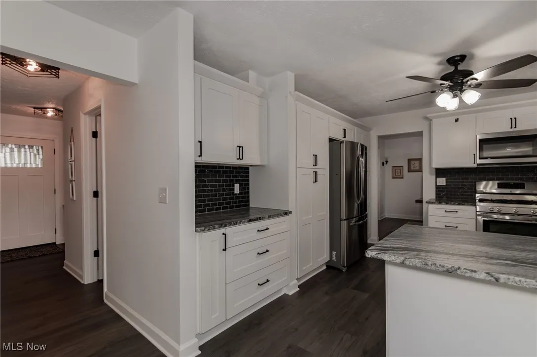 Kitchen featuring dark stone countertops, appliances with stainless steel finishes, white cabinetry, tasteful backsplash, and a textured ceiling