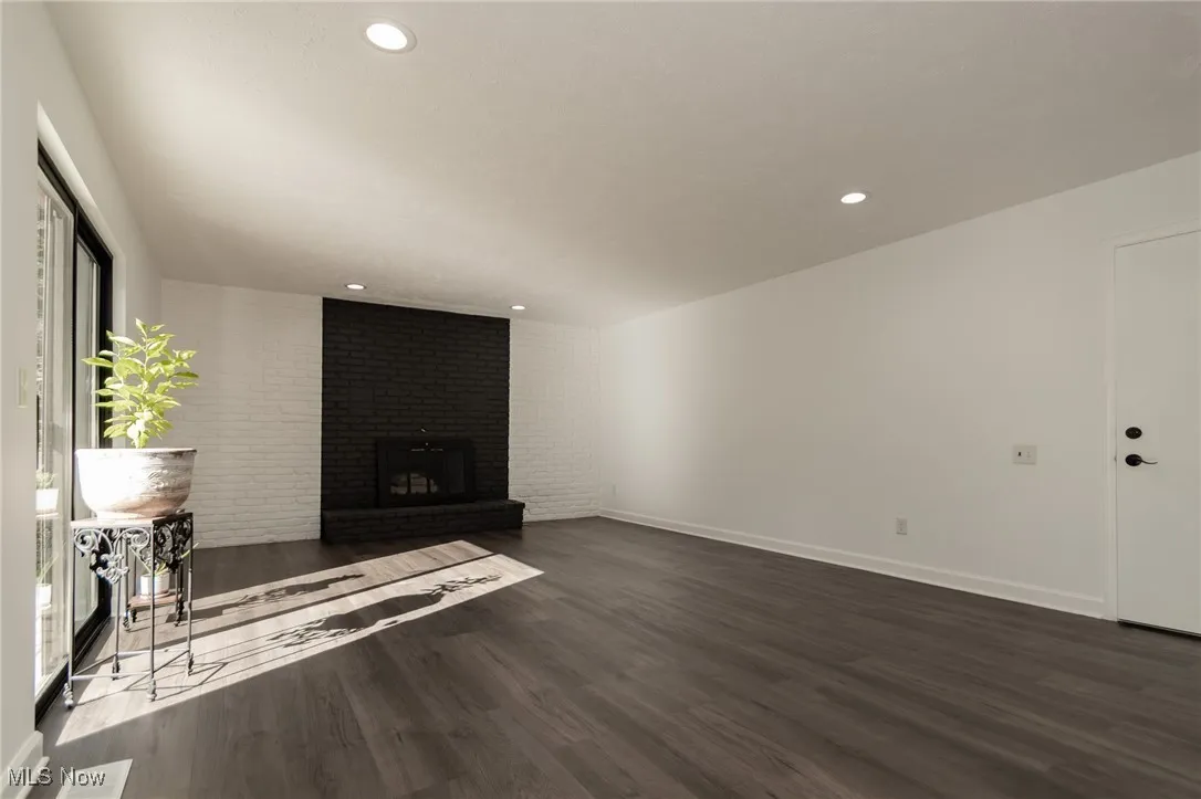 Unfurnished living room with dark wood-style floors, recessed lighting, and a brick fireplace