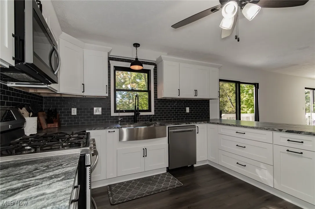 Kitchen featuring appliances with stainless steel finishes, backsplash, dark stone countertops, and white cabinets