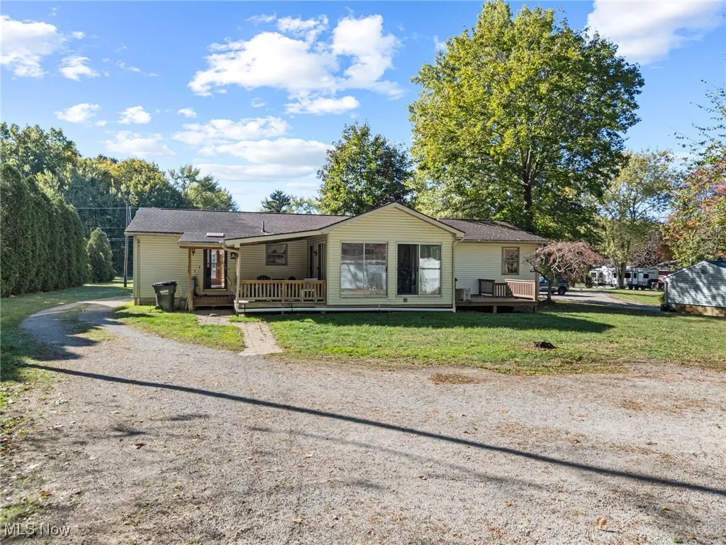 View of front of property with a wooden deck, gravel driveway, and a front lawn