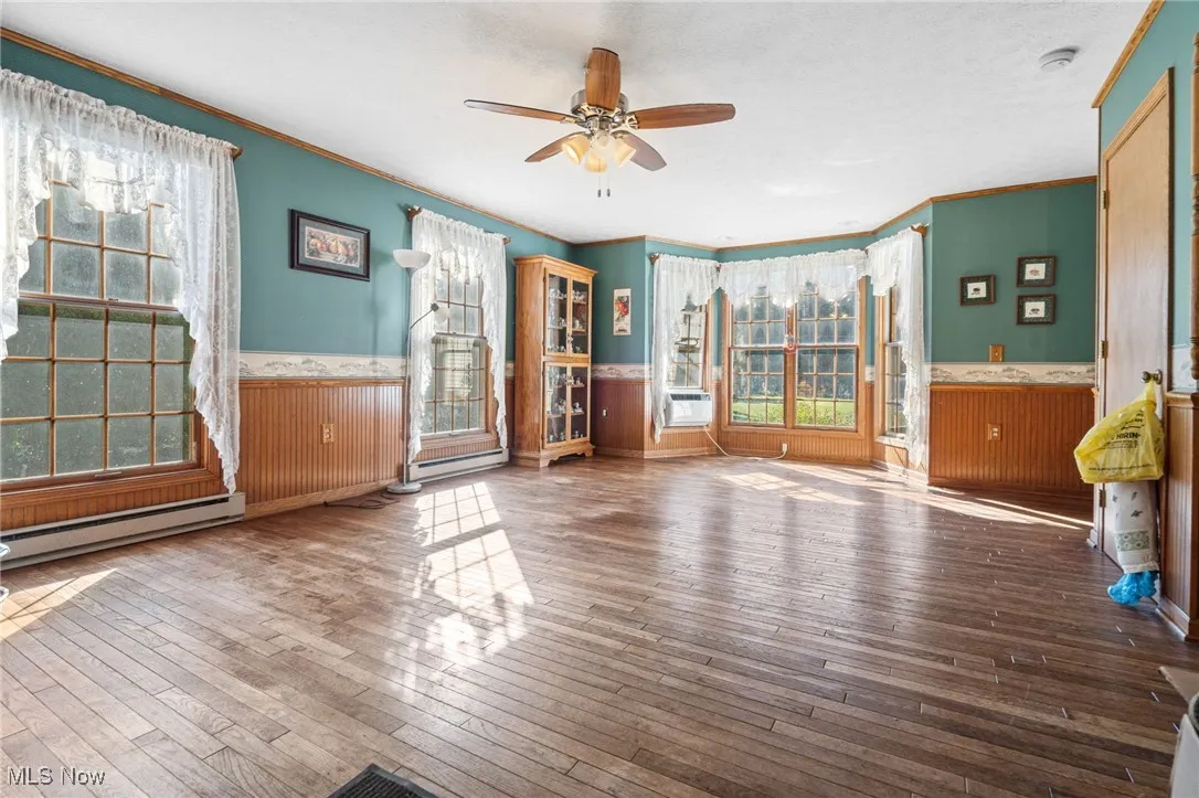 Unfurnished living room with wainscoting, ornamental molding, hardwood / wood-style floors, ceiling fan, and wood walls