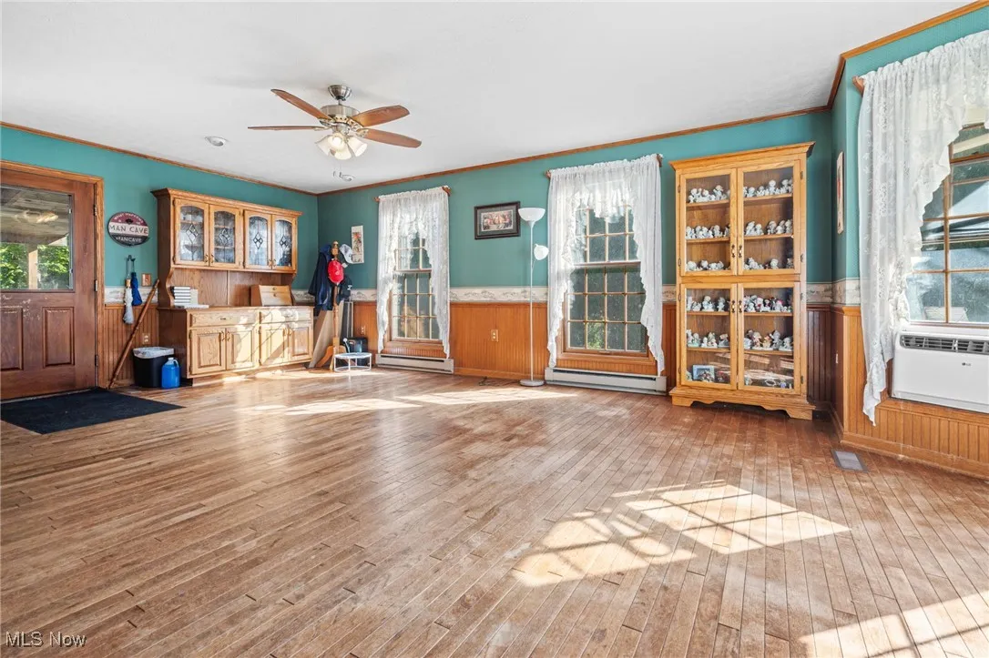 Exercise area with wood walls, wainscoting, ornamental molding, plenty of natural light, and ceiling fan