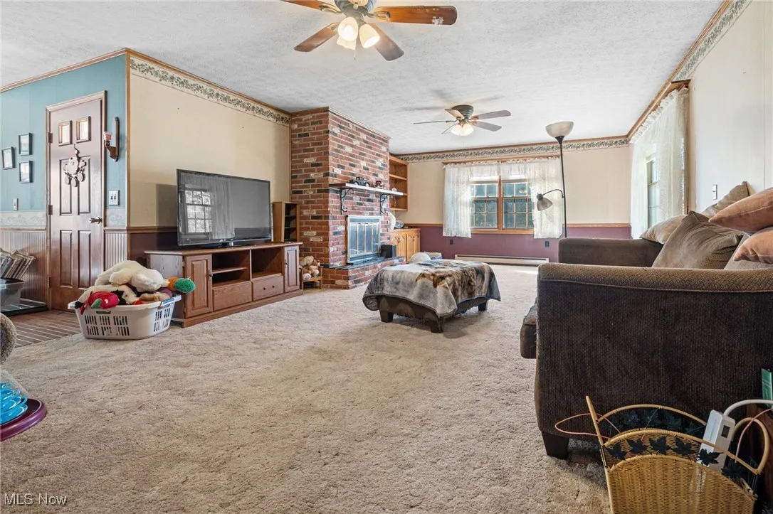 Carpeted living area with wainscoting, a textured ceiling, ornamental molding, a brick fireplace, and wooden walls