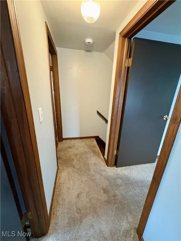 Hall with an upstairs landing, lofted ceiling, and carpet flooring