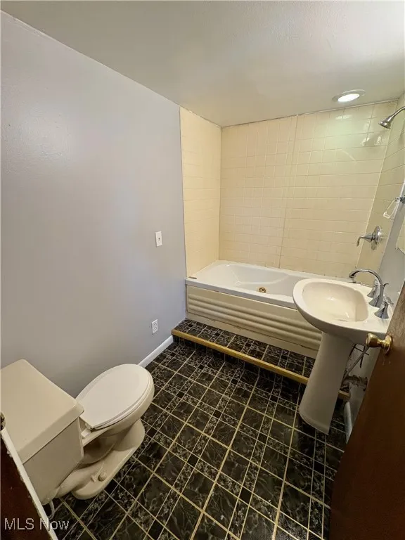 Bathroom with a combined bath / shower with jetted tub and dark tile patterned flooring