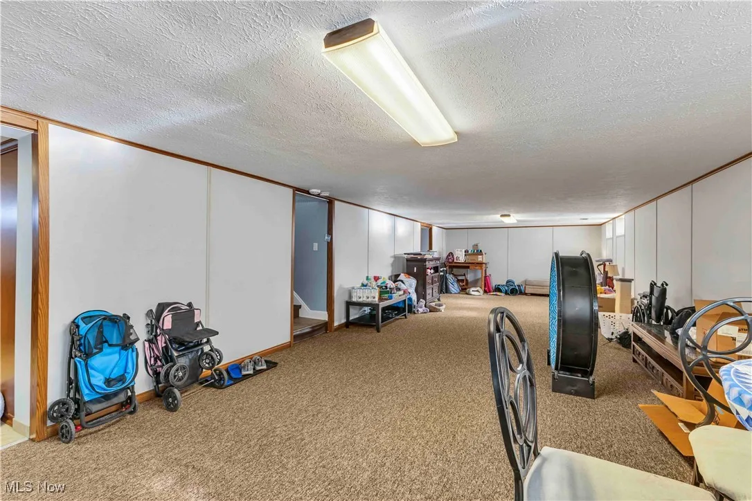 Finished basement with carpet flooring, a decorative wall, stairway, a textured ceiling, and crown molding