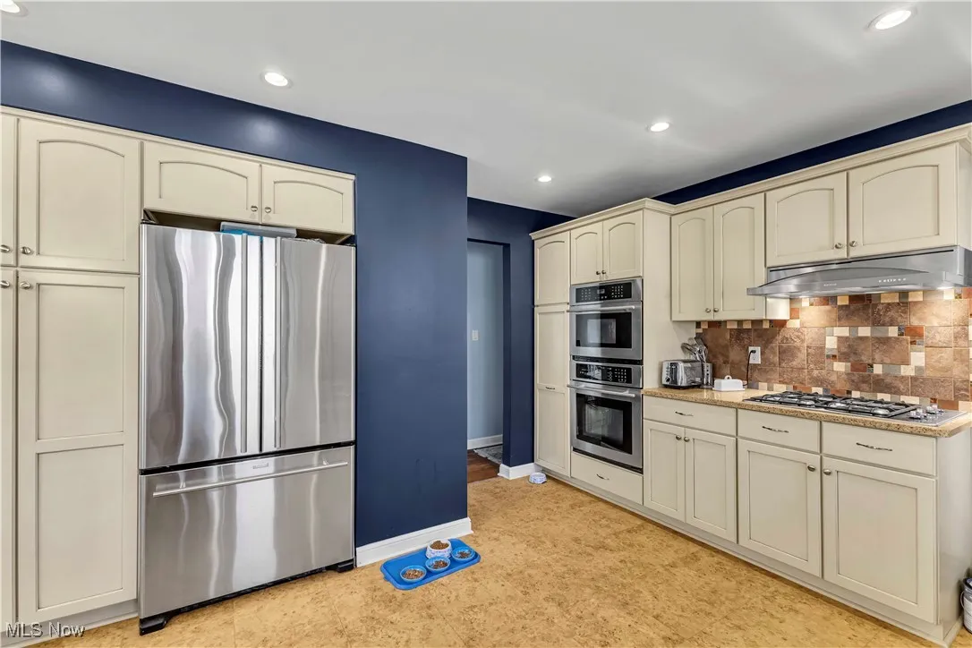 Kitchen featuring cream cabinets, stainless steel appliances, backsplash, recessed lighting, and under cabinet range hood