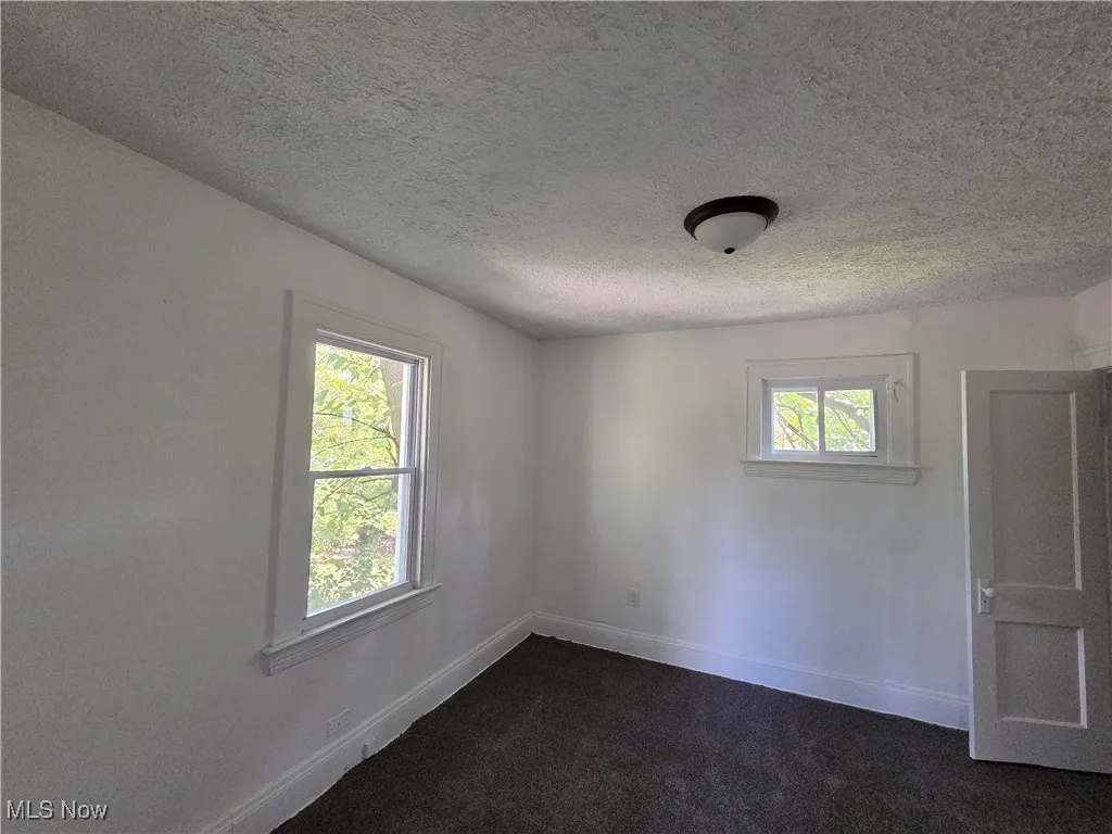 Spare room featuring healthy amount of natural light, a textured ceiling, and dark carpet
