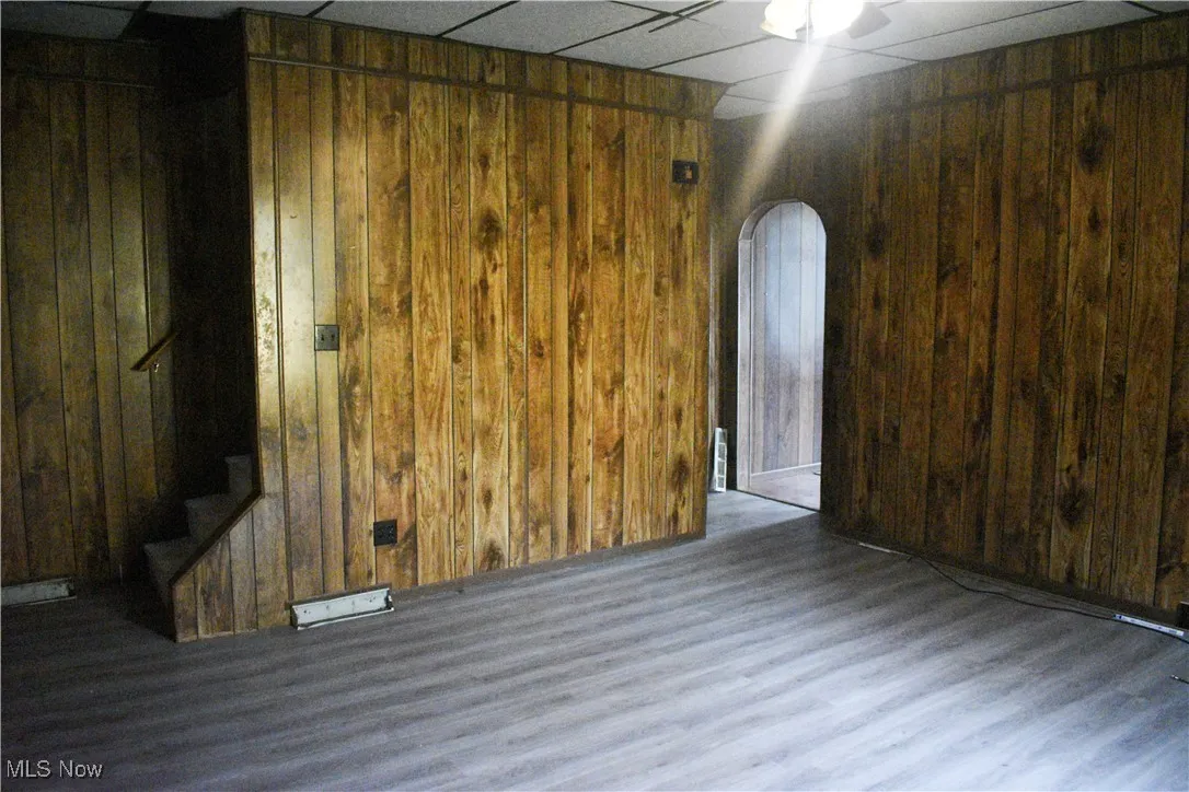 Unfurnished room featuring a paneled ceiling, wooden walls, arched walkways, stairway, and wood finished floors