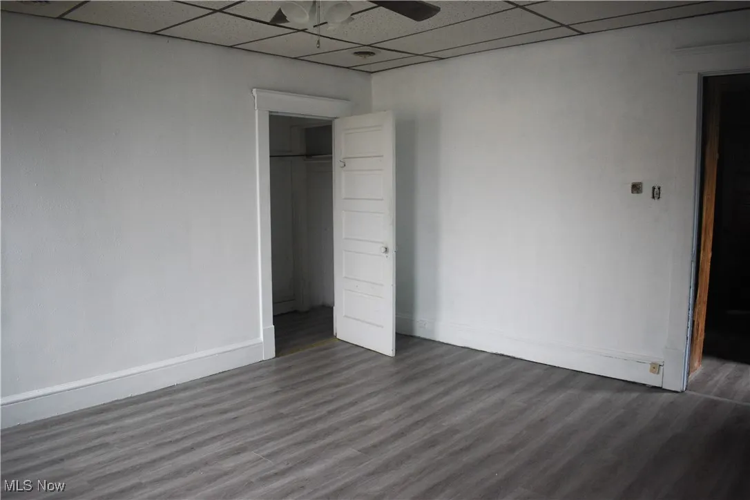 Unfurnished bedroom with a paneled ceiling, dark wood-type flooring, a closet, and a ceiling fan
