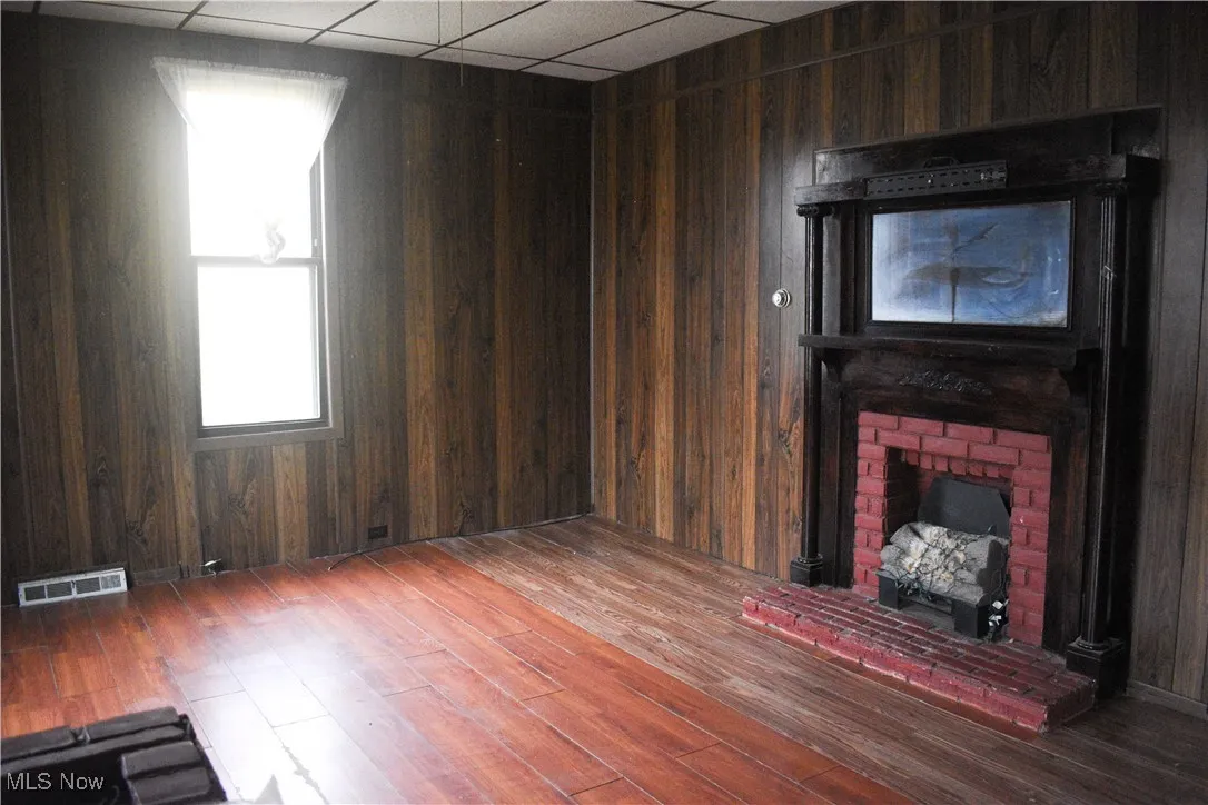 Unfurnished living room with a drop ceiling, wooden walls, a fireplace, and dark wood-type flooring