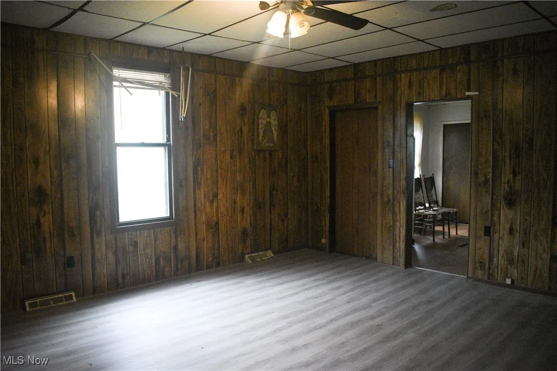 Spare room with a paneled ceiling, wooden walls, wood finished floors, and a ceiling fan