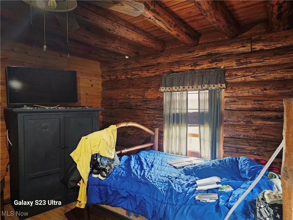Bedroom featuring a wooden ceiling with exposed beams, wood finished floors, and log walls