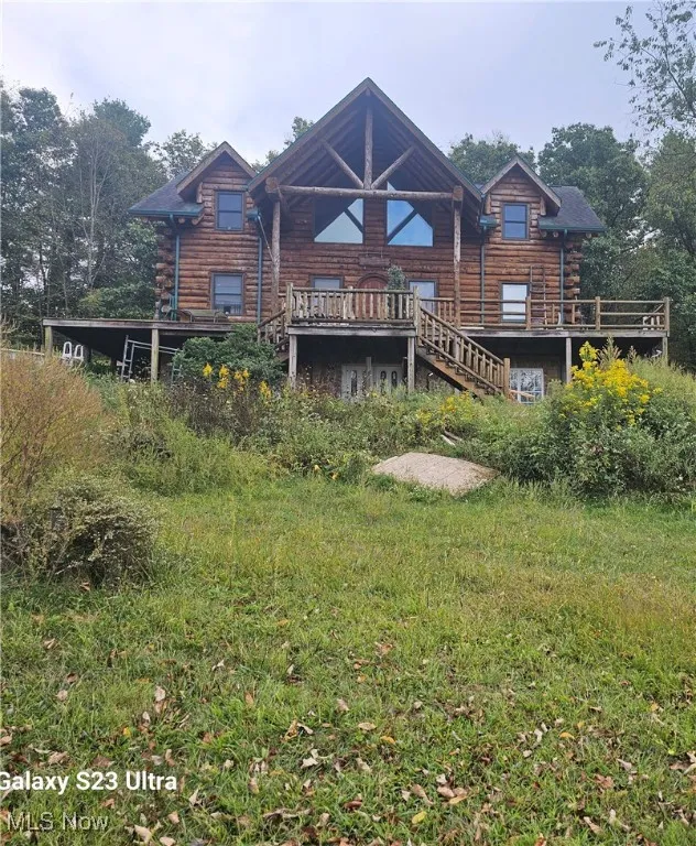 Front view of house featuring a wooden deck, log siding, and stairs