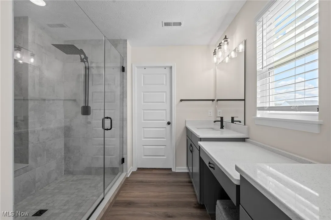 Full bath with a stall shower, vanity, a textured ceiling, and dark wood-type flooring