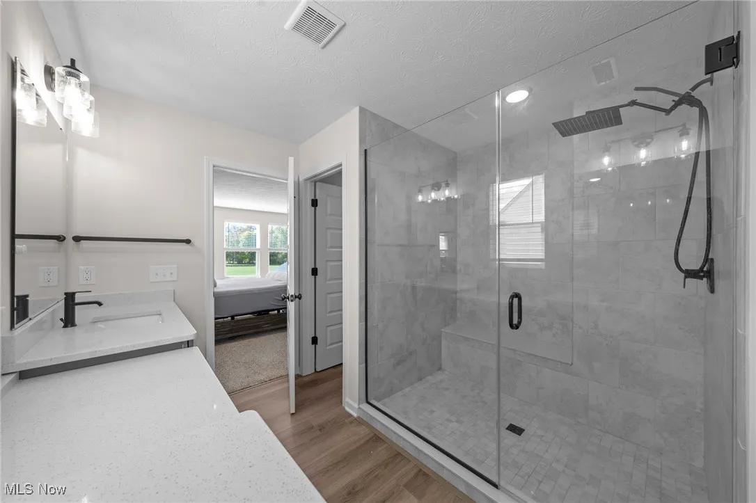 Ensuite bathroom with a shower stall, a textured ceiling, vanity, and light wood-type flooring