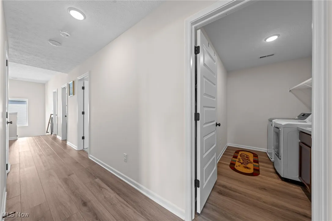Hallway with dark wood finished floors, a textured ceiling, recessed lighting, an upstairs landing, and washer and clothes dryer