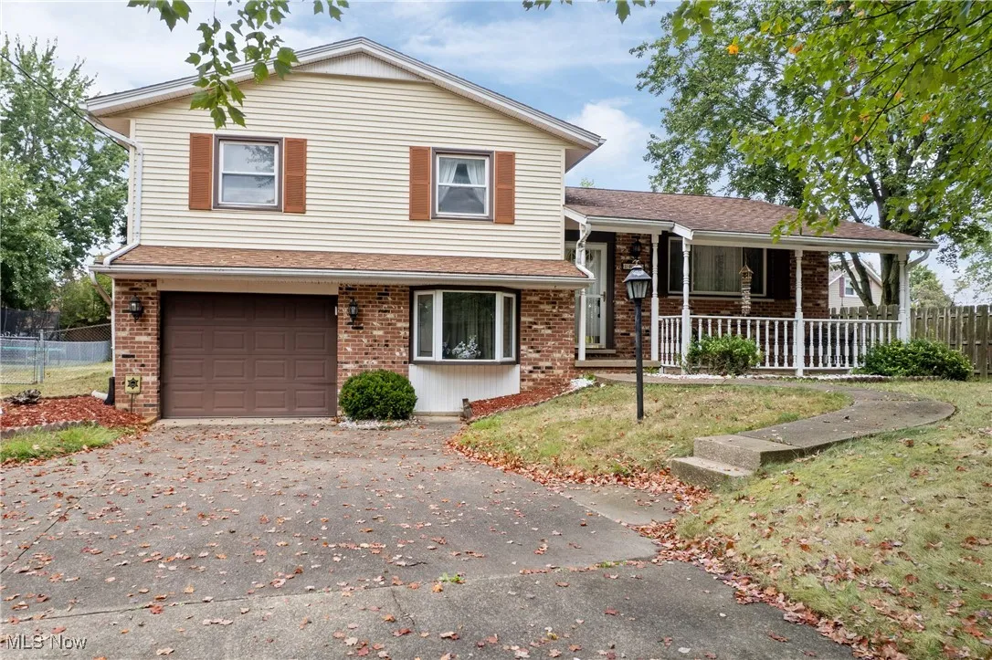 Split level home with an attached garage, driveway, brick siding, and a porch