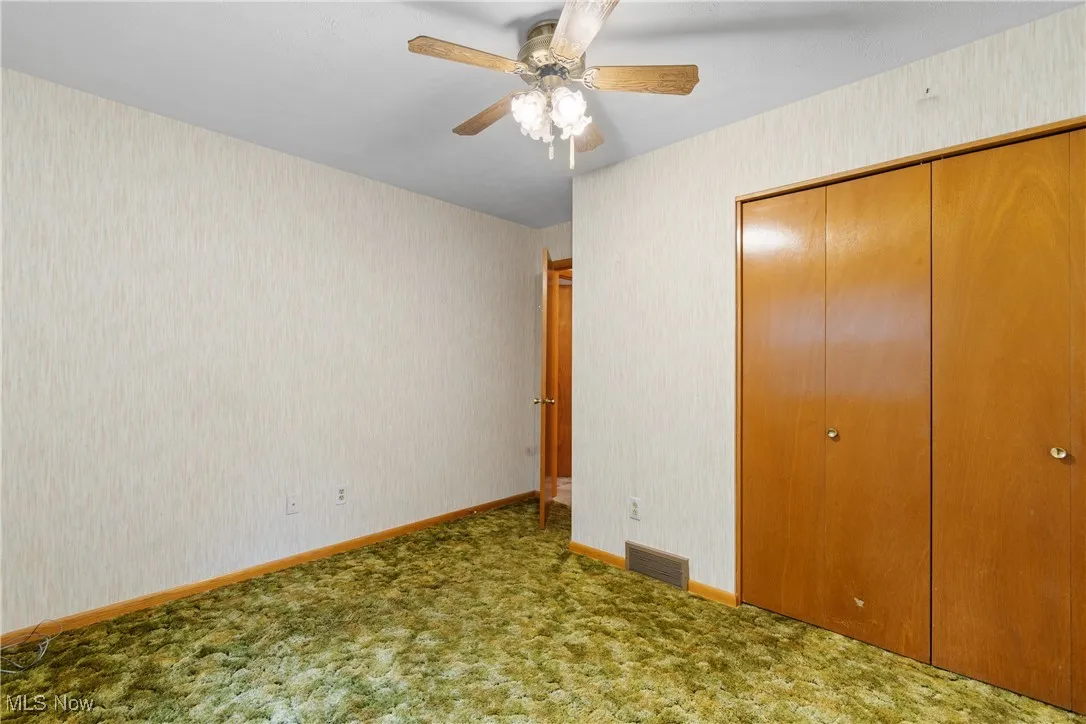Unfurnished bedroom with wallpapered walls, a closet, ceiling fan, and carpet