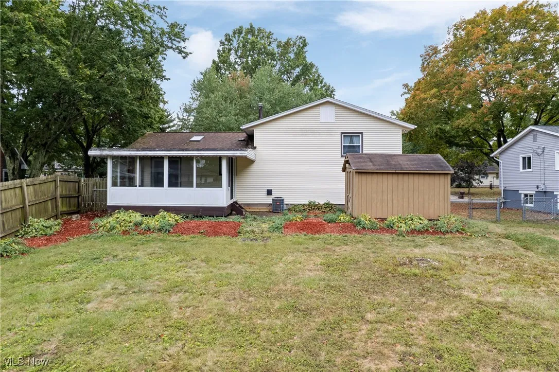 Back of house featuring a fenced backyard, a sunroom, and a storage shed