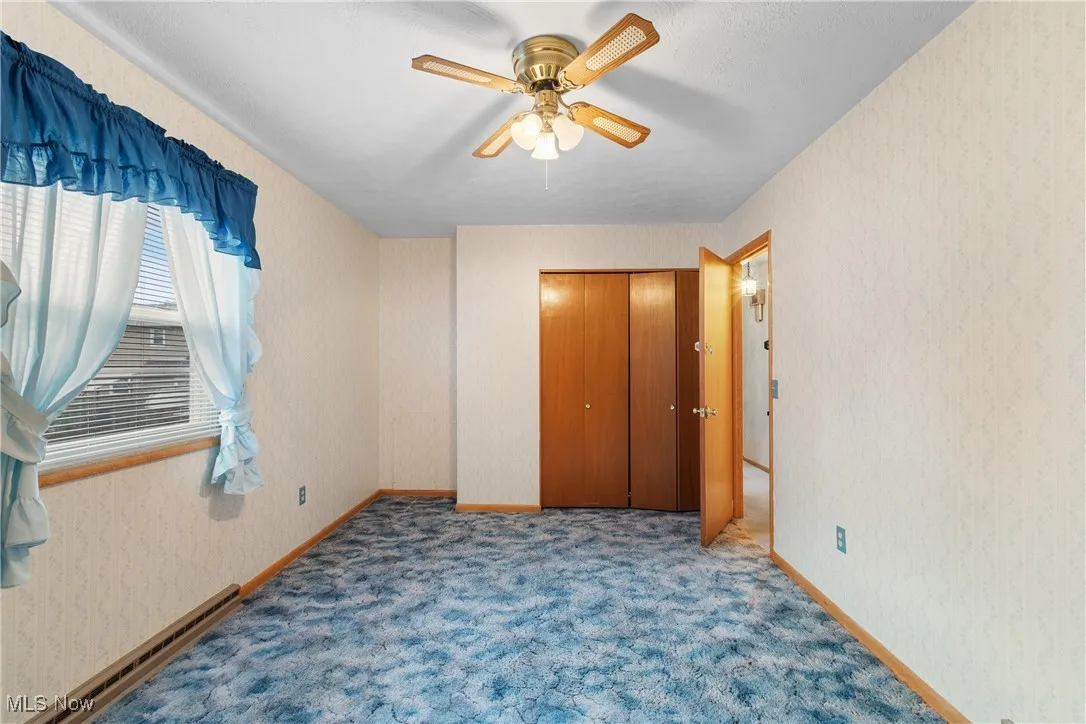 Unfurnished bedroom featuring wallpapered walls, a baseboard radiator, a ceiling fan, carpet, and a closet