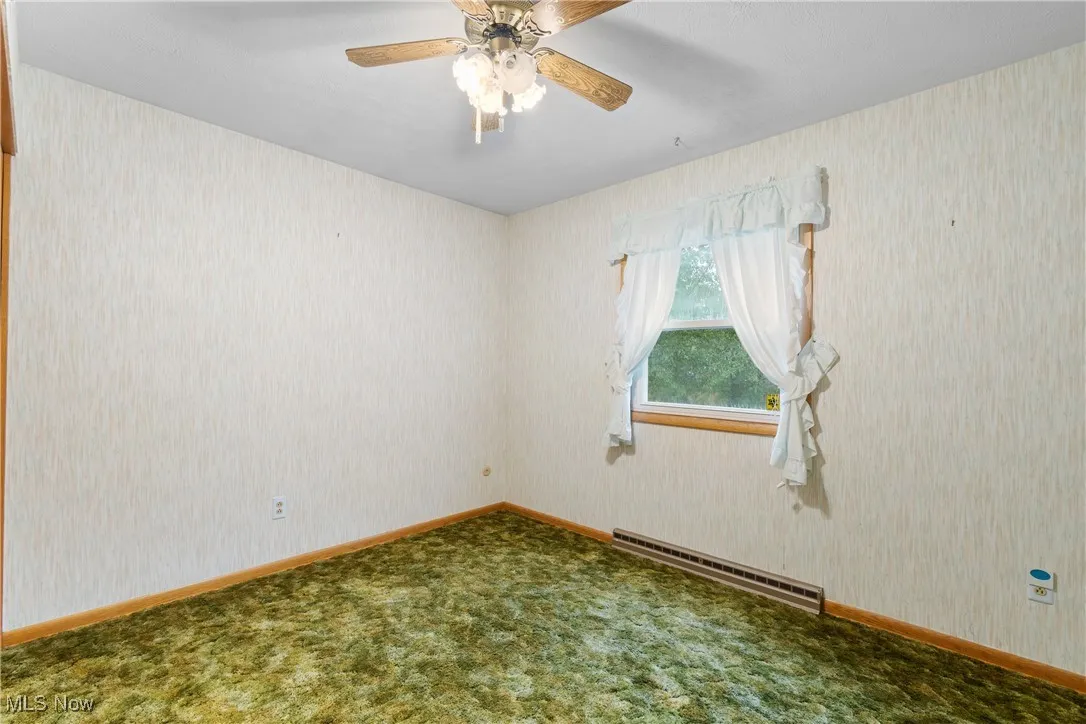 Spare room featuring wallpapered walls, baseboard heating, carpet flooring, and ceiling fan