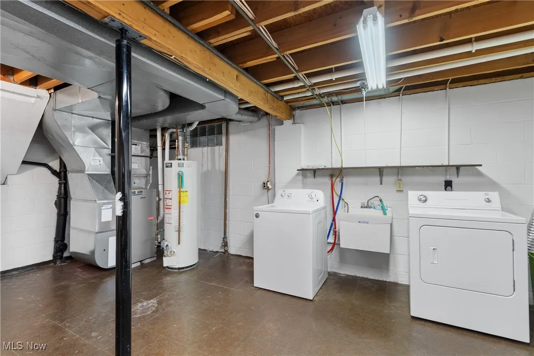 Unfinished basement featuring gas water heater, washer and clothes dryer, heating unit, and dark flooring