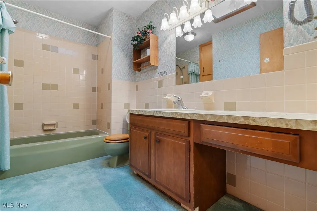 Bathroom featuring wallpapered walls, vanity, tile walls, and shower / tub combo