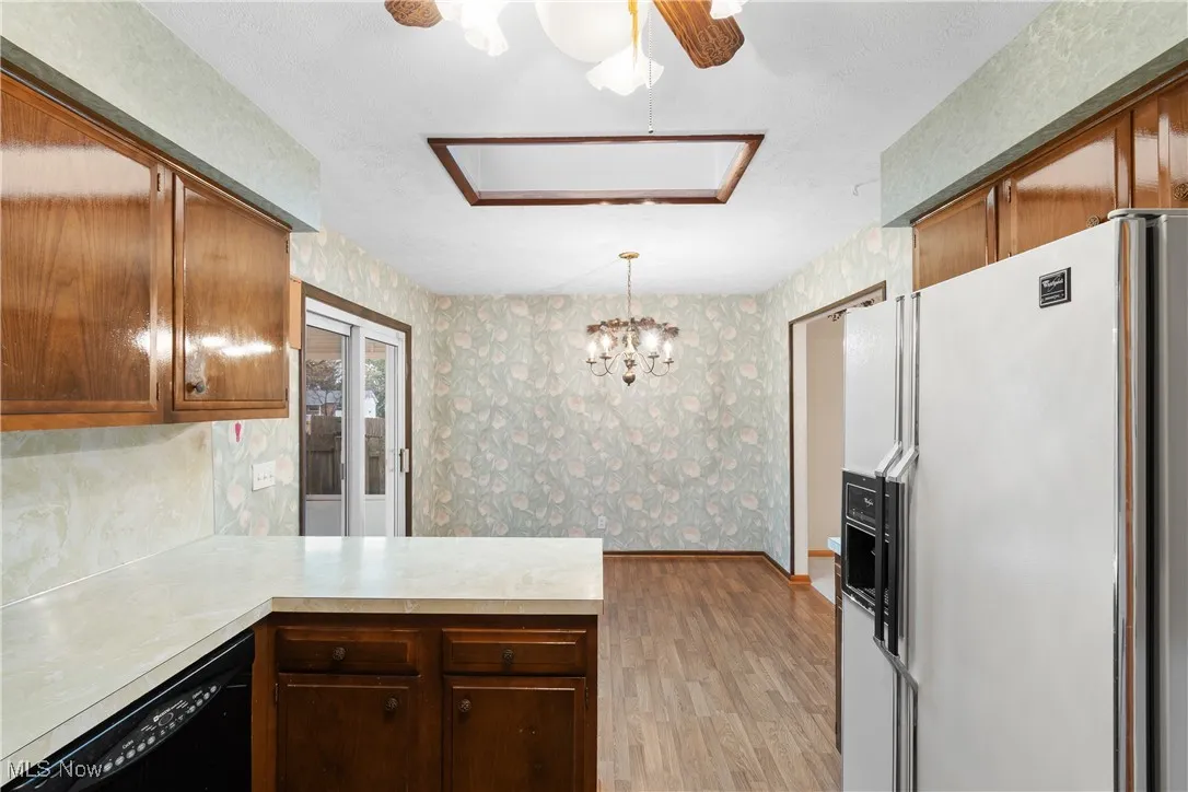 Kitchen with wallpapered walls, white refrigerator with ice dispenser, light countertops, a peninsula, and black dishwasher